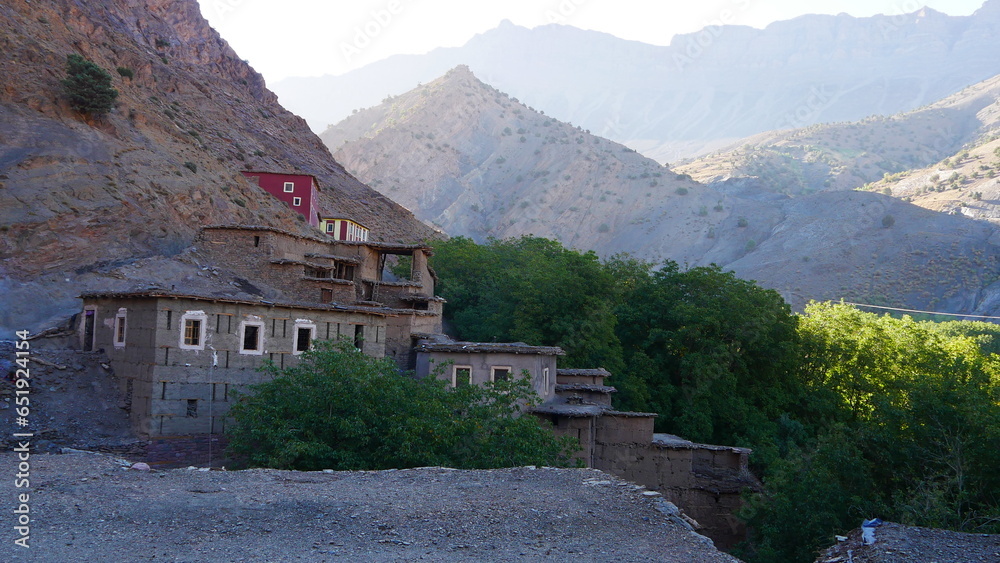 Traversé d'un village berbère sur le flanc d'une montagne, chaîne Atlas, jeu d'éclairage de Soleil et d'ombre, zone désertique et rocailleuse, un peu de végétation, construction en pierre historique, 