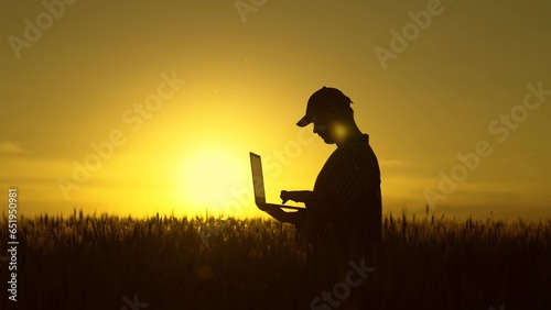 Agronomist works in field. Modern concept of agricultural business, Businessman with laptop in his hands works in wheat field, communicates and checks harvest. Farmer at sunset with computer.
