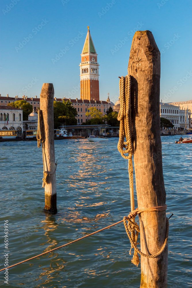 Piazza San Marco, Venice, Italy, Romantic walk in Venice at sunshine. Wooden stakes on the canal grande in venice. St Mark’s Square Campanile in the background. - obrazy, fototapety, plakaty 