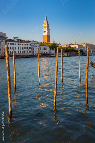 Romantic walk in Venice at sunset. Wooden stakes on the canal grande in venice, St Mark’s Square Campanile in the background. Piazza San Marco, Venice, Italy photo