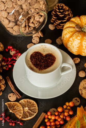 Autumn-themed composition with cup of coffee in the middle, decorated with coco heart. Autumn leaves, pumpkin, jar of cookies. © Nikola