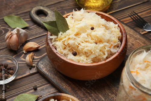 Bowl with delicious sauerkraut and different spices on wooden background