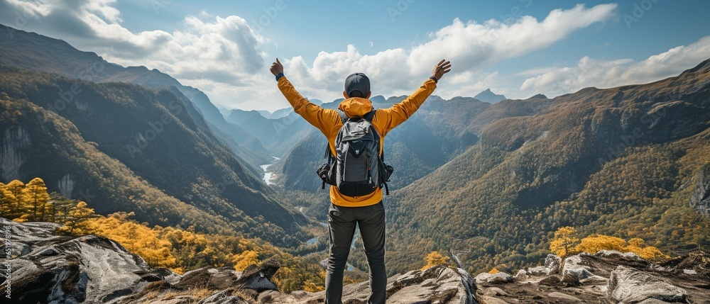 Back view of a young Asian hiker standing and raising his hands in happiness on the summit of a rough mountain, copy space. - obrazy, fototapety, plakaty 