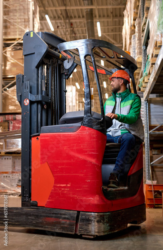 man in protective safety jumpsuit uniform in hardhat at warehouse works with forklift loader. Portrait of professional forklift driver in factory's warehouse. logistics, transportation industrial