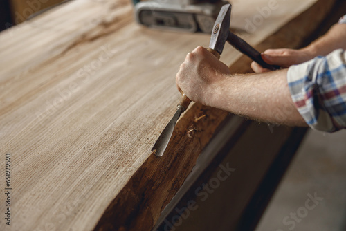 Close up of craftsman working with chisel while cutting wooden plank in carpentry workshop photo