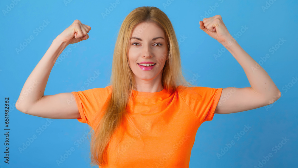 Fototapeta premium Arm, bicep and woman for fun, sport, health and fitness. Happy smiling female lady showing bicep muscle with confident expression, strength power. Studio shot isolated on blue background