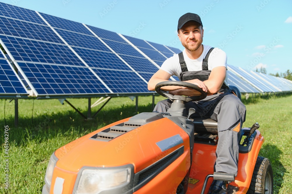 A man working at solar power station. A worker on a garden tractor mows grass on a solar panel farm.