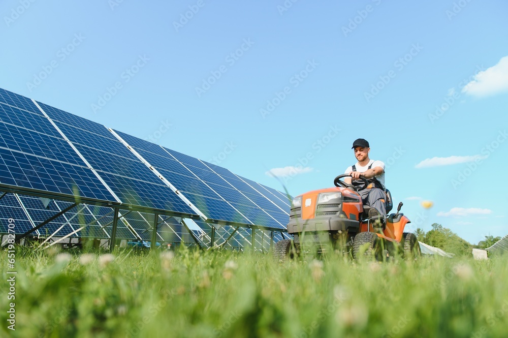 A man drives a lawnmower near solar panels. Concept of solar energy A man drives a lawnmower near solar panels. Concept of solar energy