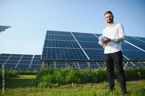 Positive bearded male investor standing against photovoltaic panels producing alternative energy. © Serhii