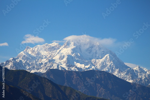 Under the blue sky, the mountains are covered with snow and clouds are circling the mountain © Asad