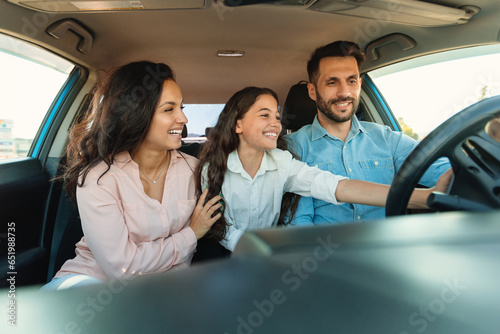 Tableau sur toile Happy parents and their child enjoying brand new car, girl touching wheel, sitti