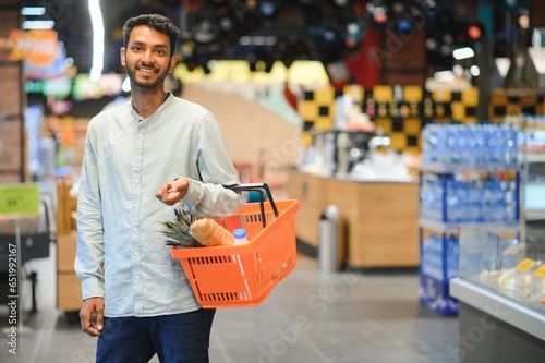 Portrait of handsome young Indian man standing at grocery shop or supermarket, Closeup. Selective Focus.