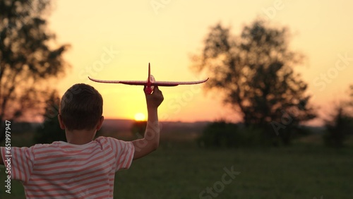 Boy wants to become pilot, astronaut. Slow motion. Happy kid runs with toy airplane on field in sunset light. Children play toy airplane. Teenager dreams of flying and becoming pilot. Child aviator