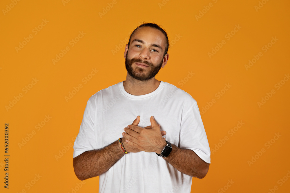 Serious calm millennial european man with beard in white t-shirt presses hands to chest, make thanks gesture Serious calm millennial european man with beard in white t-shirt presses hands to chest, make thanks gesture