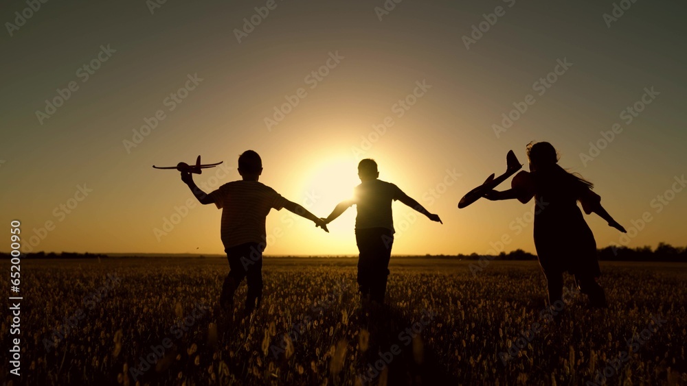 Children play with toy plane. Happy children run with toy plane across field at sunset. Boy, girl wants to become pilot, astronaut. Slow motion. Teenager dreams of flying, becoming pilot. Silhouette