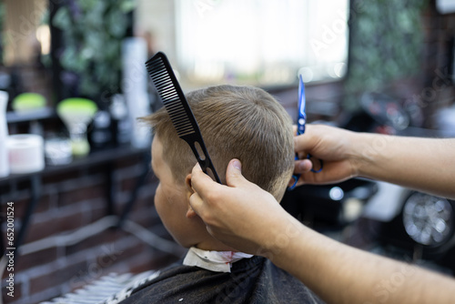 In a hairdressing salon, a child sits in a chair and carefully observes the work of a hairdresser. The child loves to get a haircut and is not afraid of the hairdresser. Haircut concept. photo