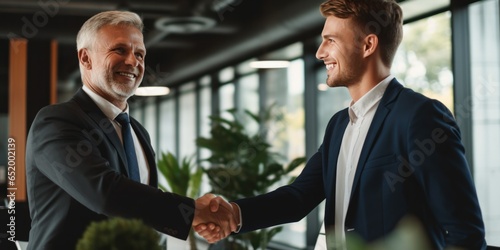 Success In Business And Career Is Illustrated As A Young Man Smiles And Shakes Hands With A European Businessman After A Successful Negotiation Or Interview In An Office Setting photo