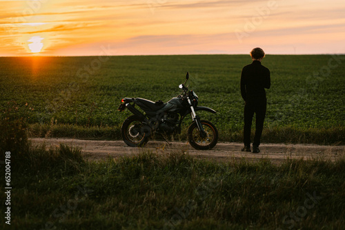 male motorcyclist on a country road with an enduro motorcycle at sunset.
