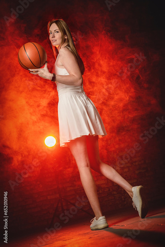 Young girl with the basketball ball posing on the red color smoke background.