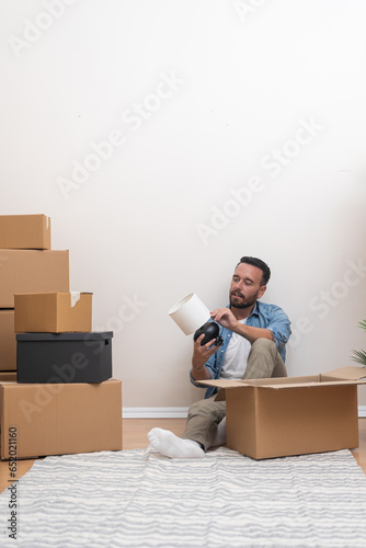 A bearded young man, laptop in use, embraces a fresh start in his new apartment amid the chaos of unpacked boxes photo