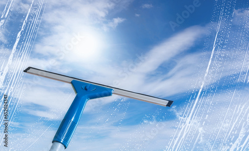 Foto Rubber squeegee cleans a soaped window and clears a stripe of bright blue sky, s