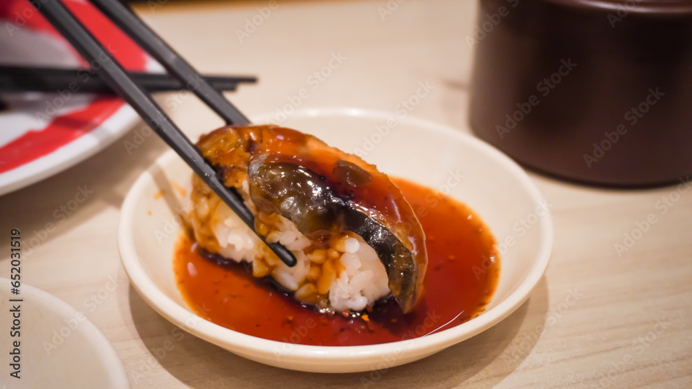Close up photo of someone dipping sushi in soy sauce using chopsticks on Japanese Restaurant. Concept for whole healthy food, nutrition, omega-3, animal protein, seafood, modern resto and street food.