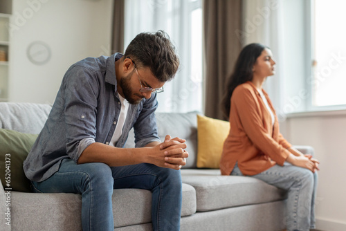 Unhappy indian man and woman sitting on sofa, husband and wife feeling down after quarrel, spouses thinking about divorce, need for family therapy photo