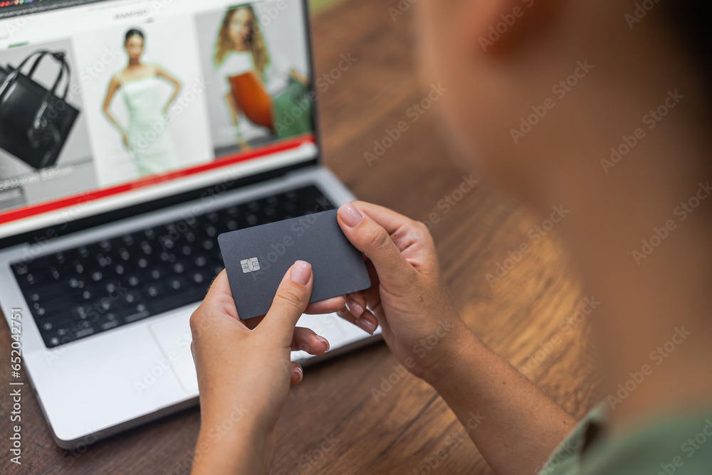Delicate hands hold a credit card against a laptop screen displaying an online fashion clothing store's website, exemplifying seamless online shopping. 