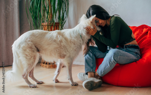 Animal, pet, dog, adoption, shelter, socialized, rescued. Young happy stylish woman plays with her fluffy white dog at home