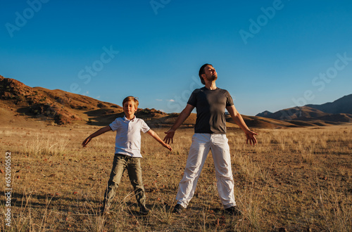 Father and son enjoying nature standing with their eyes closed in the mountains