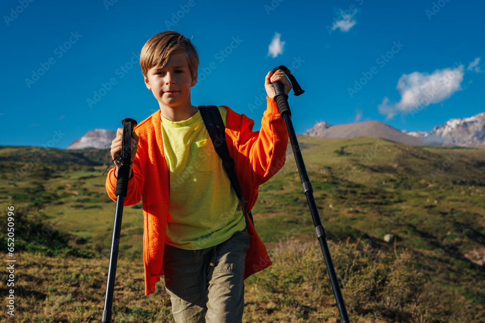Boy hiker with backpack and trekking poles walking in the mountains