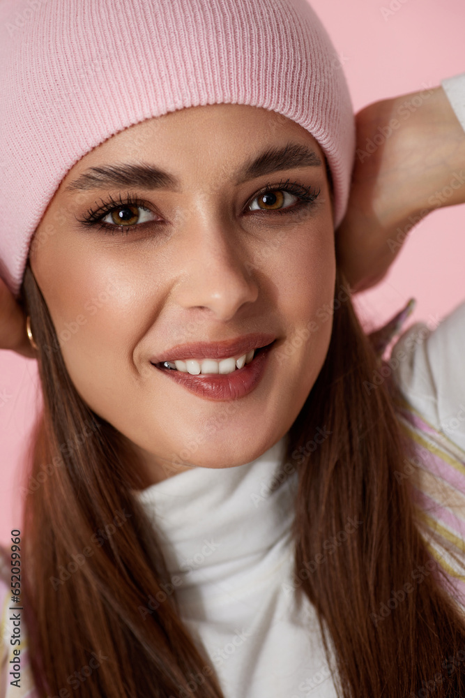 playful woman keeps hands on pink hat on pink background. playful woman keeps hands on pink hat on pink background.