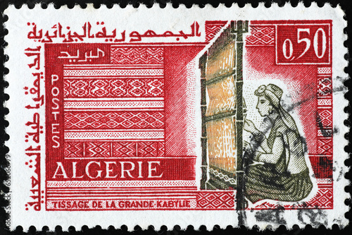 Woman creating a carpet at the loom on algerian stamp photo