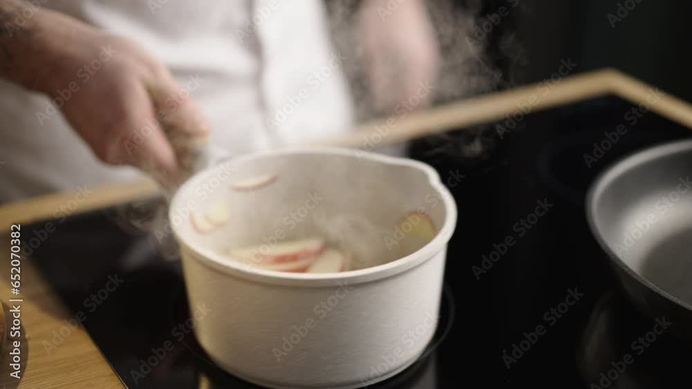 Hand of unrecognizable male cook stirring apple slices sauteing with butter in saucepan Hand of unrecognizable male cook stirring apple slices sauteing with butter in saucepan