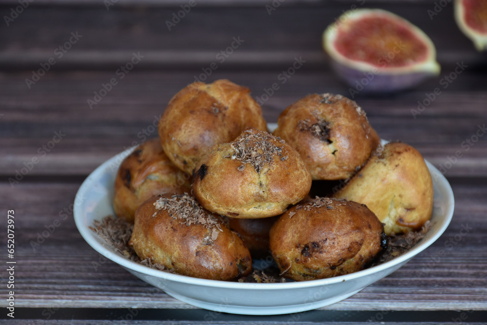 Delicious homemade profiteroles cakes with cocoa cream filling and chocolate chips. Choux pastry, cream puffs on plate, fig halves on wooden table background. 