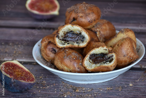 Delicious homemade profiteroles cakes with cocoa cream filling and chocolate chips. Choux pastry, cream puffs halved on plate, fig halves on wooden table background. 