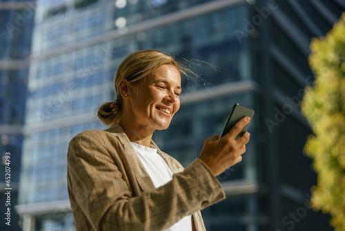 Stylish woman freelancer using phone whiile standing on modern building background  photo