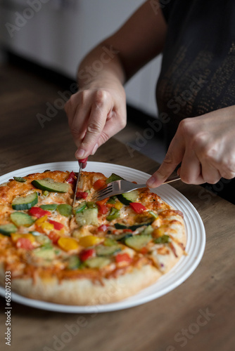 Woman cuts pizza with cutlery in the kitchen