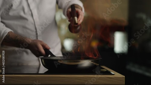 Chef doing flambe to dish in pan with large fire flame in sliced vegetables photo
