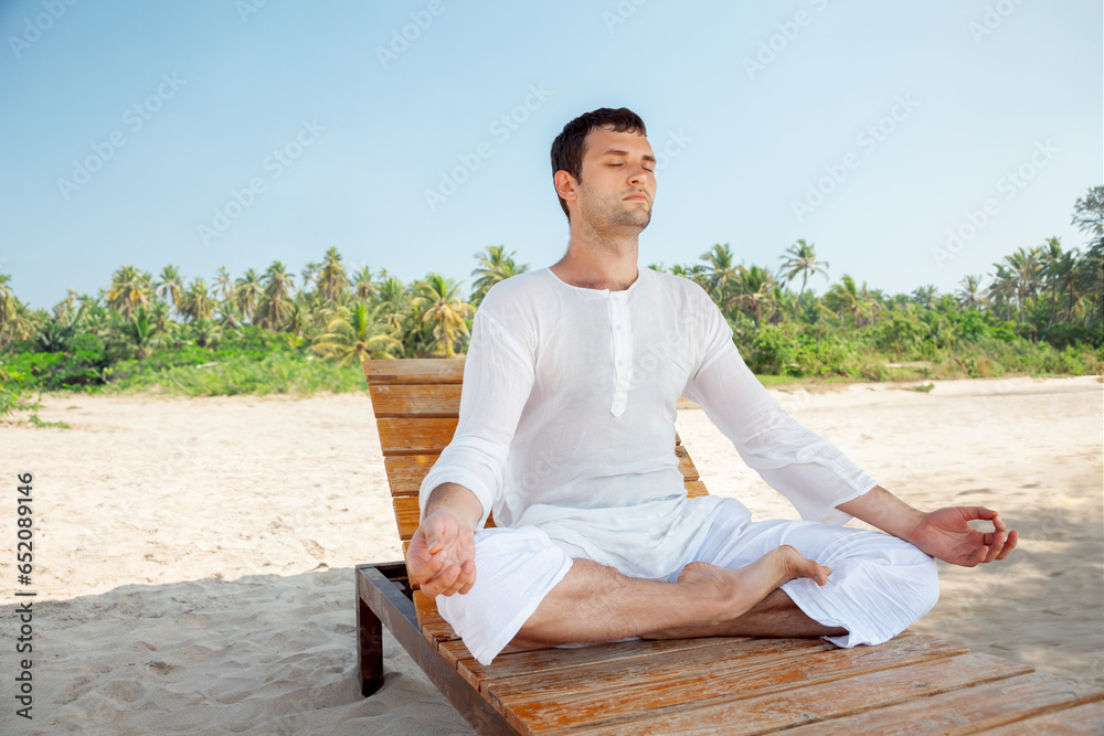 Young Adult Man Meditating on Sunny Tropical Beach