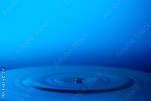 A droplet of water dispersing on a blue surface, alongside empty space for adding text.