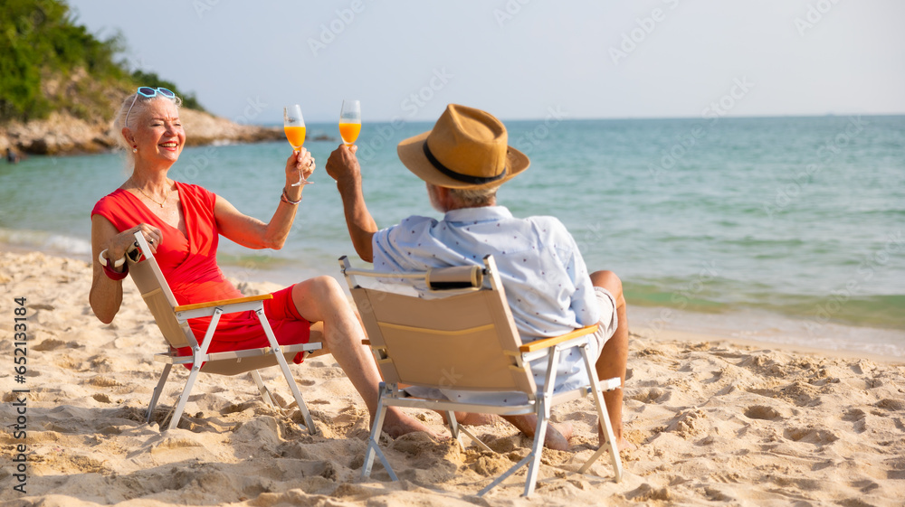 Elderly couple man and woman wearing fashion sunglasses talking together and looking at the sea sky sitting on chair on beach. Vacation trip summer holiday.