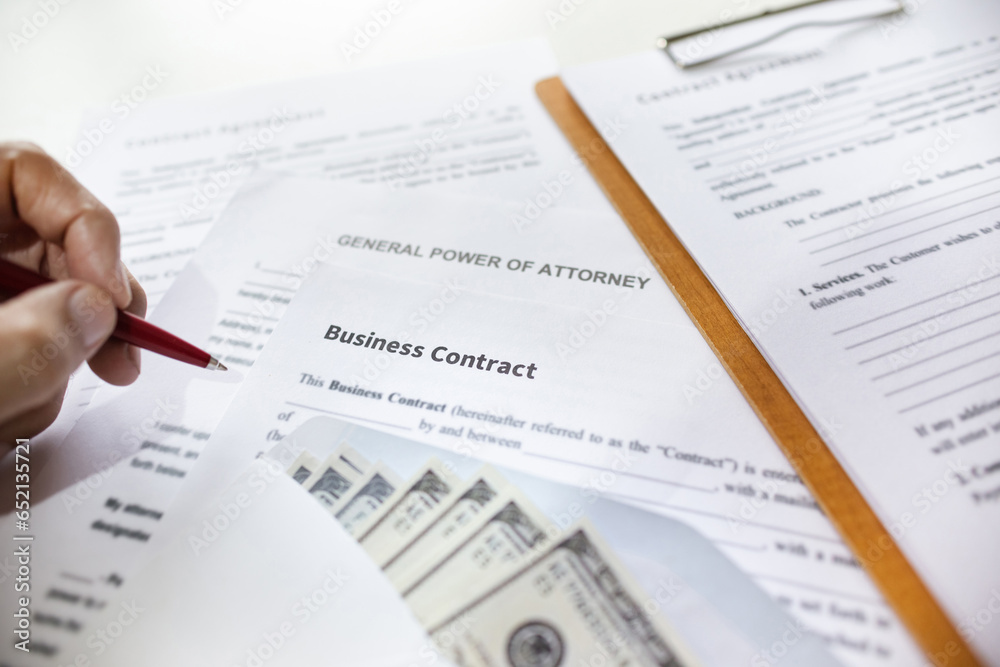 Close-up view, business contrack document with dollar in white envelope on desk and hand holding pen ready to sign contract or give power of attorney. concept about recive commission or corruption Close-up view, business contrack document with dollar in white envelope on desk and hand holding pen ready to sign contract or give power of attorney. concept about recive commission or corruption