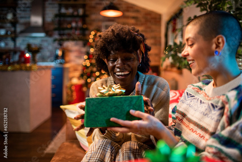 Young interracial lesbian couple gifting presents during christmas and the new year holidays at home photo