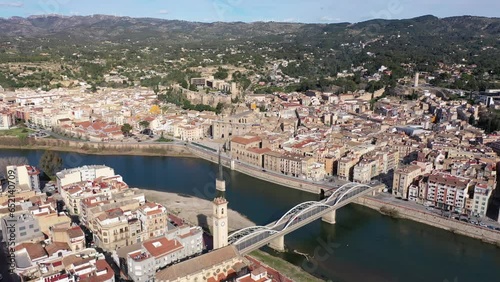 Scenic view from drone of Tortosa cityscape on banks of Ebro river with State Bridge and Ebro Battle Monument in water on sunny spring day, Spain photo