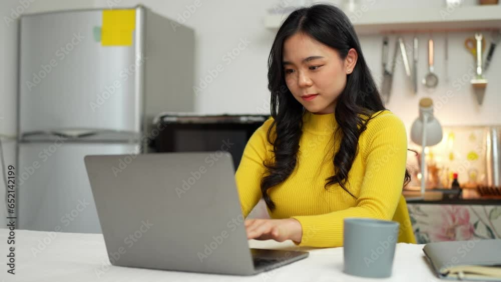 Smiling happy beautiful Asian woman relaxing using technology of laptop computer. take note of information Have a relaxing hot drink while sitting on the table in your room at home. Smiling happy beautiful Asian woman relaxing using technology of laptop computer. take note of information Have a relaxing hot drink while sitting on the table in your room at home.