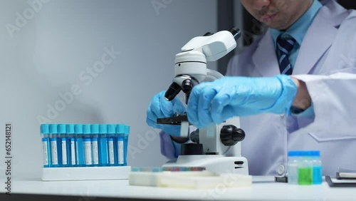 Asian scientist looking at a microscopic sample of experimental cyan is doing an in vitro vaccine experiment in a science lab. medical research concept.