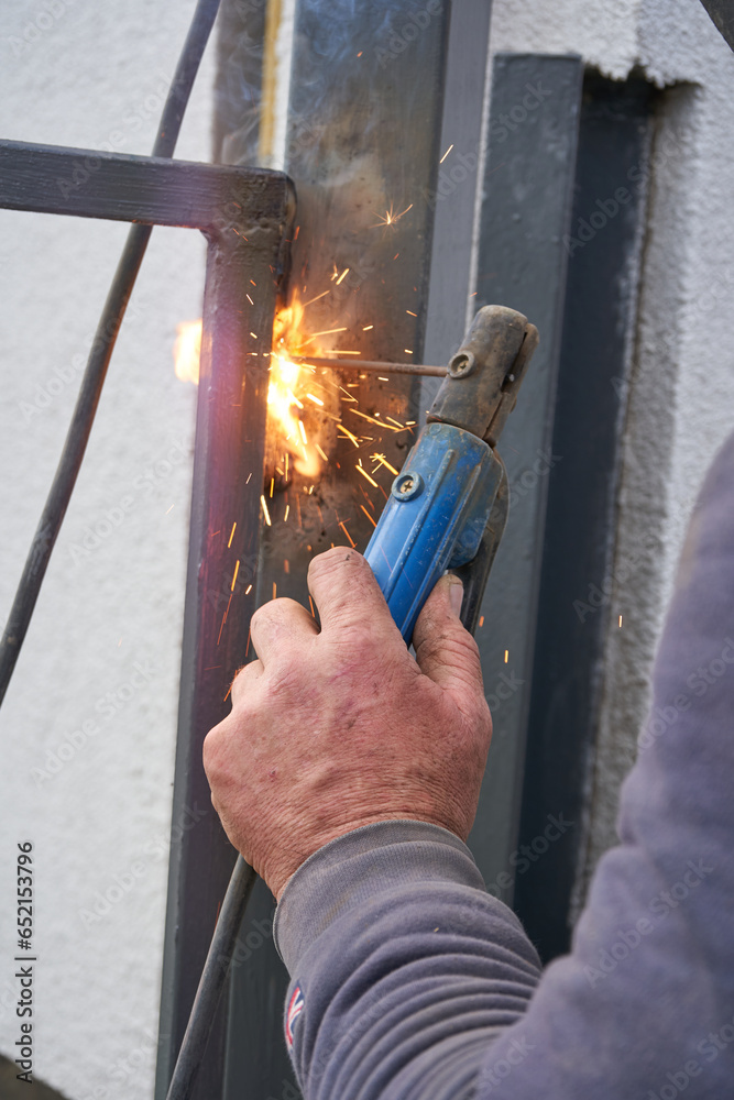 welding of a metal gate,the hand of a welder welding a hinge on a gate