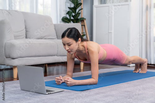 Fit young asian woman planing on the living room floor while following exercise instruction on online training video. Healthy lifestyle workout routine at home. Balance and endurance concept. Vigorous