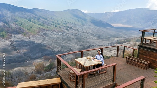 beautiful and enthusiastic asian woman using laptop and headset to work remotely on cafe balcony with mountain background.  millennial lifestyle concept working remotely and working online.